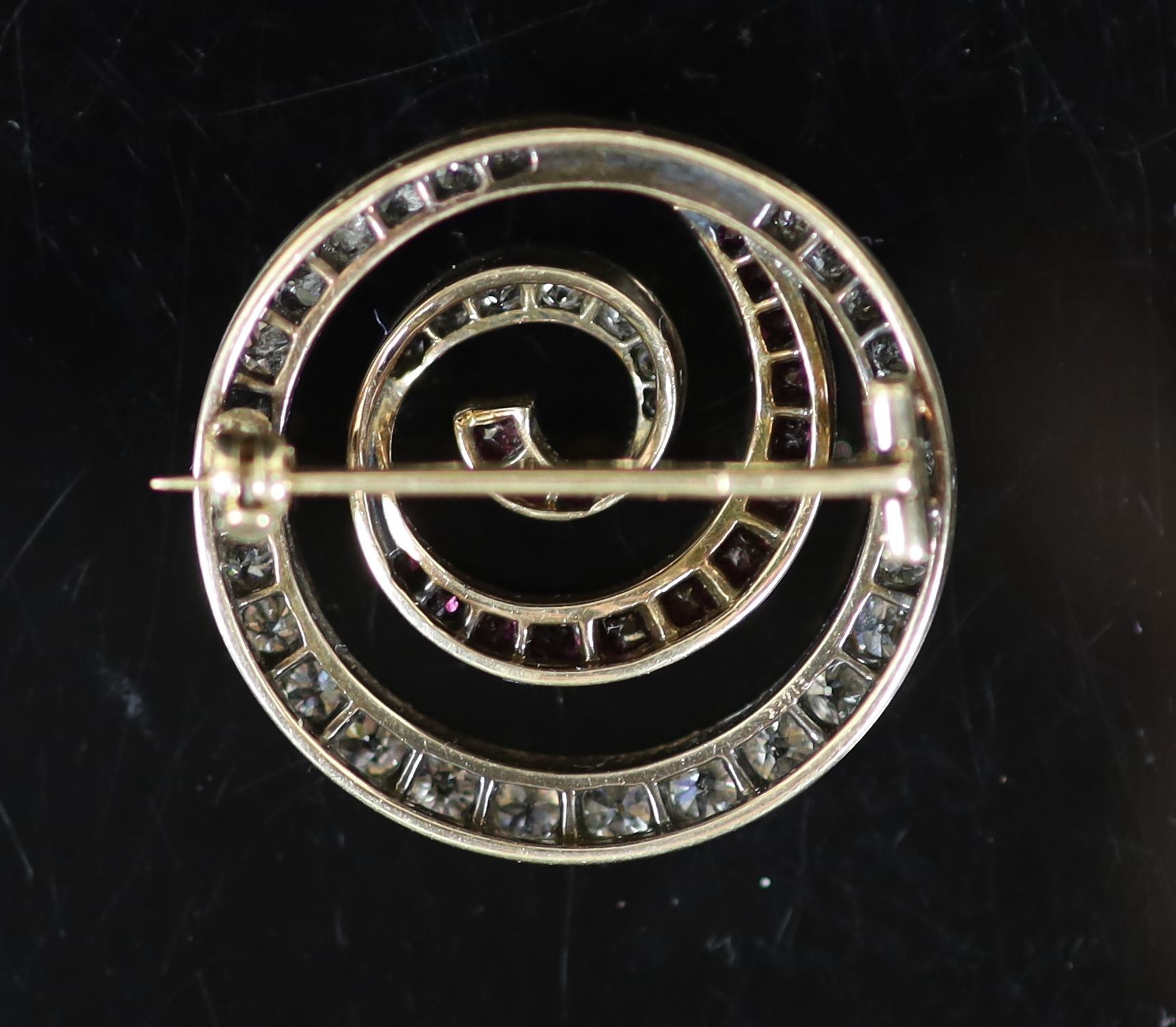 An early 20th century gold and silver, graduated ruby and diamond set open work whorl brooch